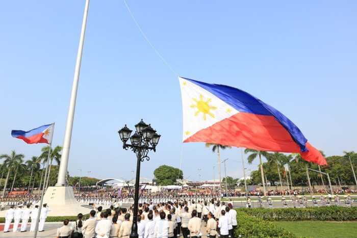 A massive Philippine flag rises over a crowd in white.